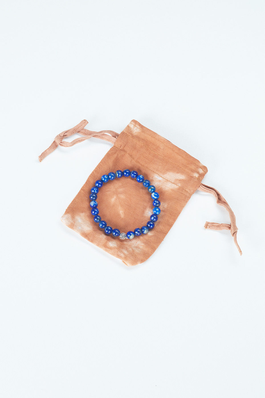 A beaded bracelet made a dark blue stone, is positioned atop a small bag made out of recycled materials. The bag is orange in color and slightly larger than the bracelet