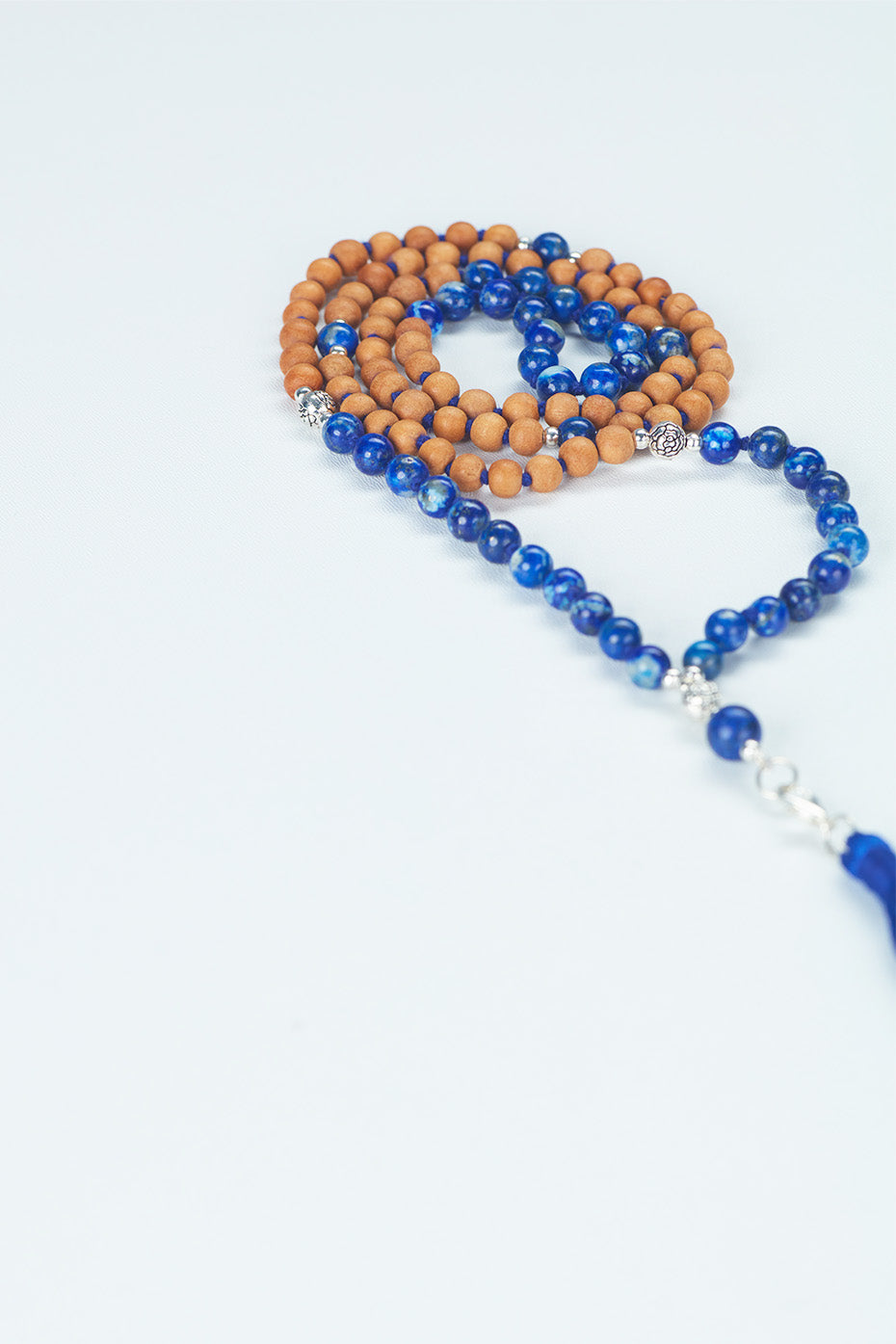 A beaded necklace, composed of Sandalwood and beads, with the wooden beads in focus as the tassels extend beyond the frame on the right side