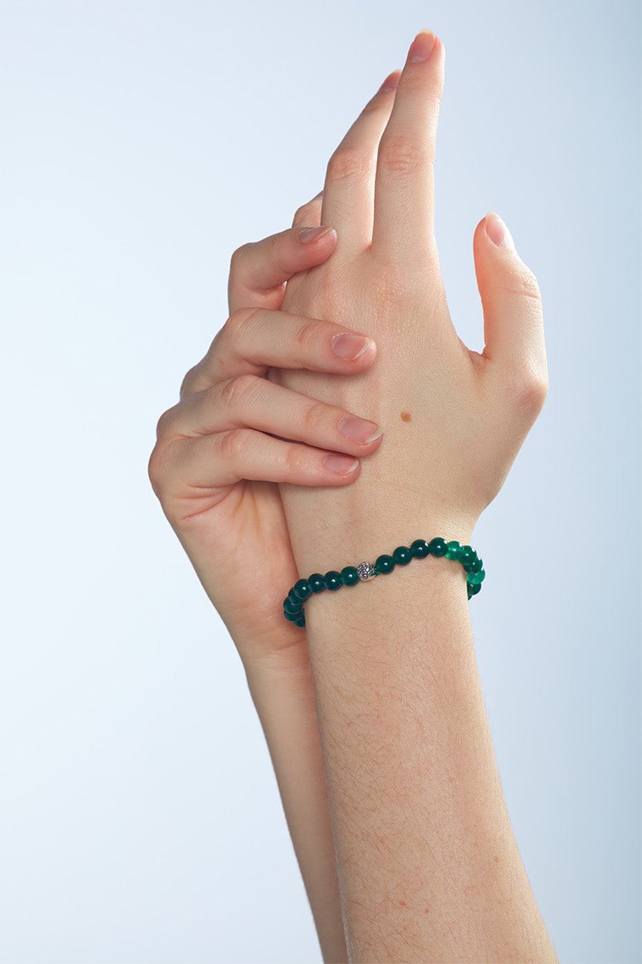  Two hands are positioned closely. On the left wrist is a beaded bracelet with beads that present as green.