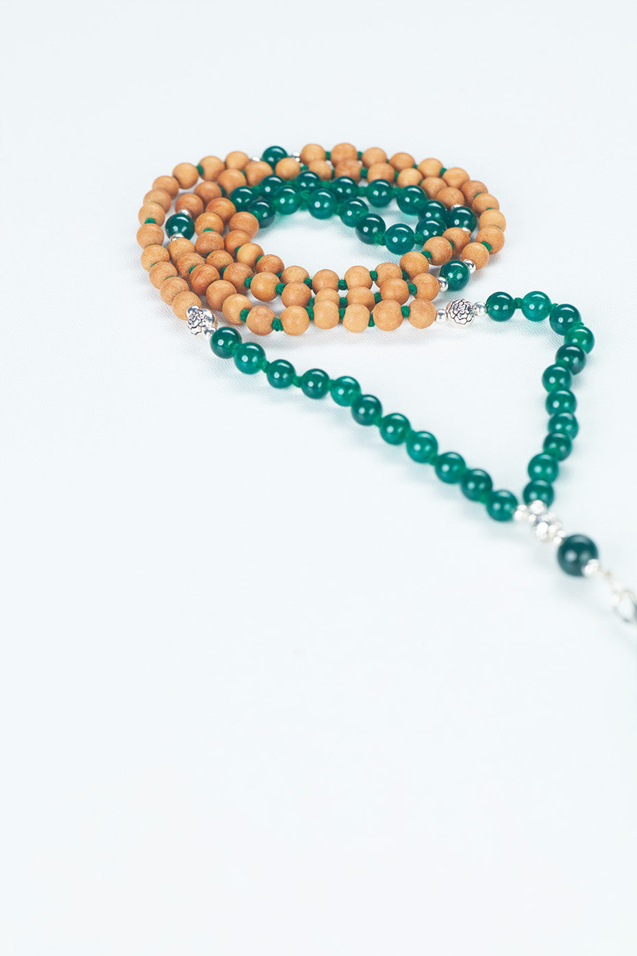 A beaded necklace, composed of Sandalwood and beads, with the wooden beads in focus as the tassels extend beyond the frame on the right side.