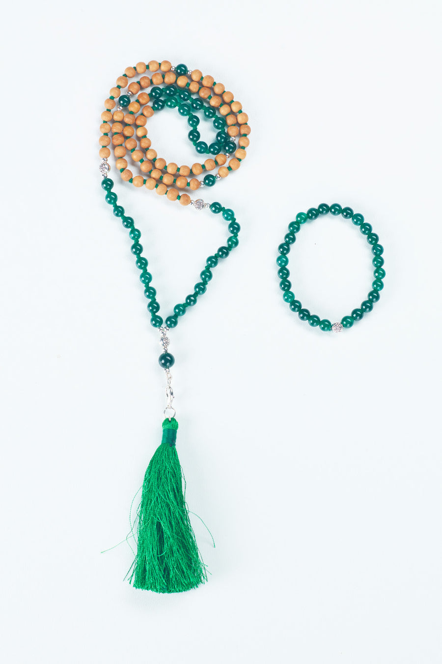 Two pieces of jewelry are shown: on the left a beaded necklace made of Sandalwood and a green stone, with a green tassel on the bottom, and on the right a beaded bracelet made of a green stone